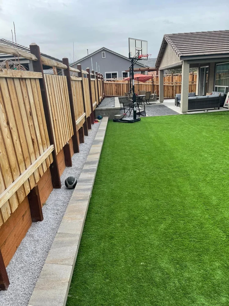 Artificial turf side yard along a wooden fence with a paver edge