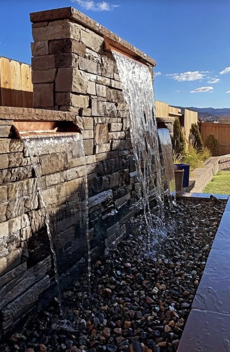 Stacked stone water wall with spillways over a bed of river rock