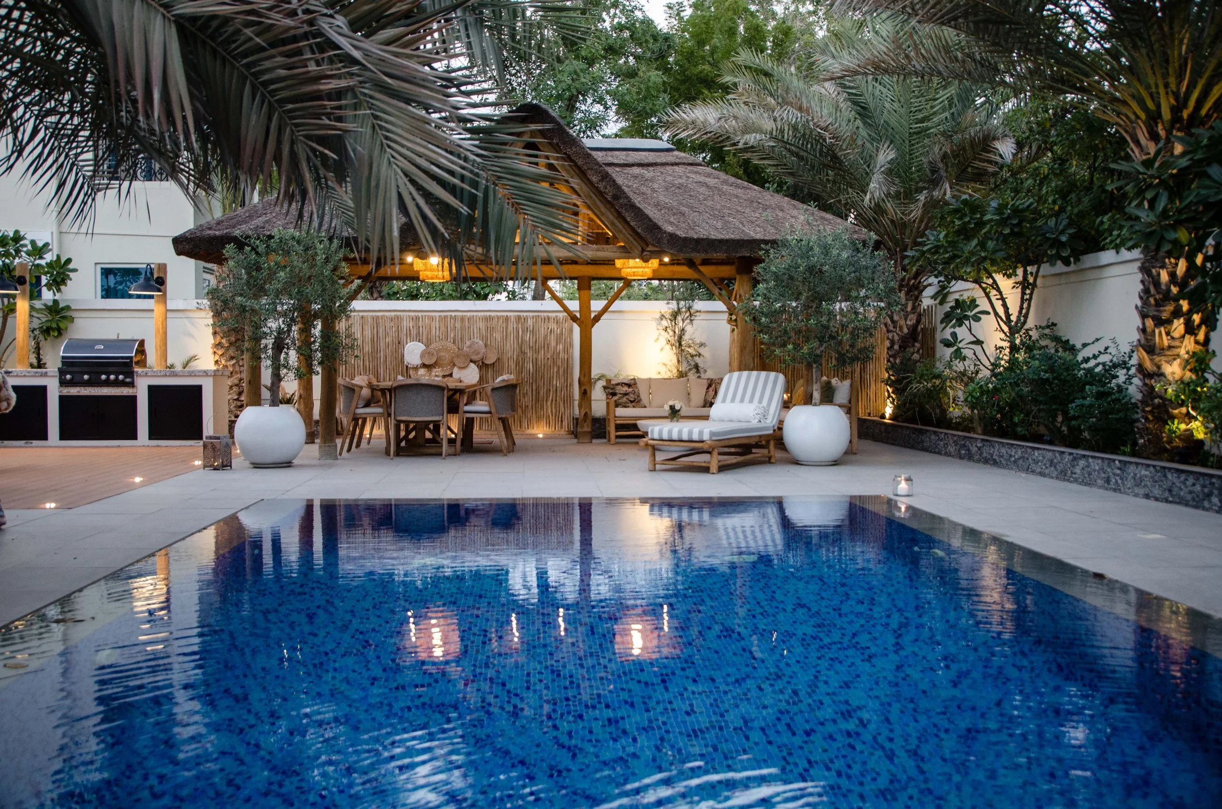 Beautiful thatched cabana meets open deck with bbq and fire pit in picturesque setting