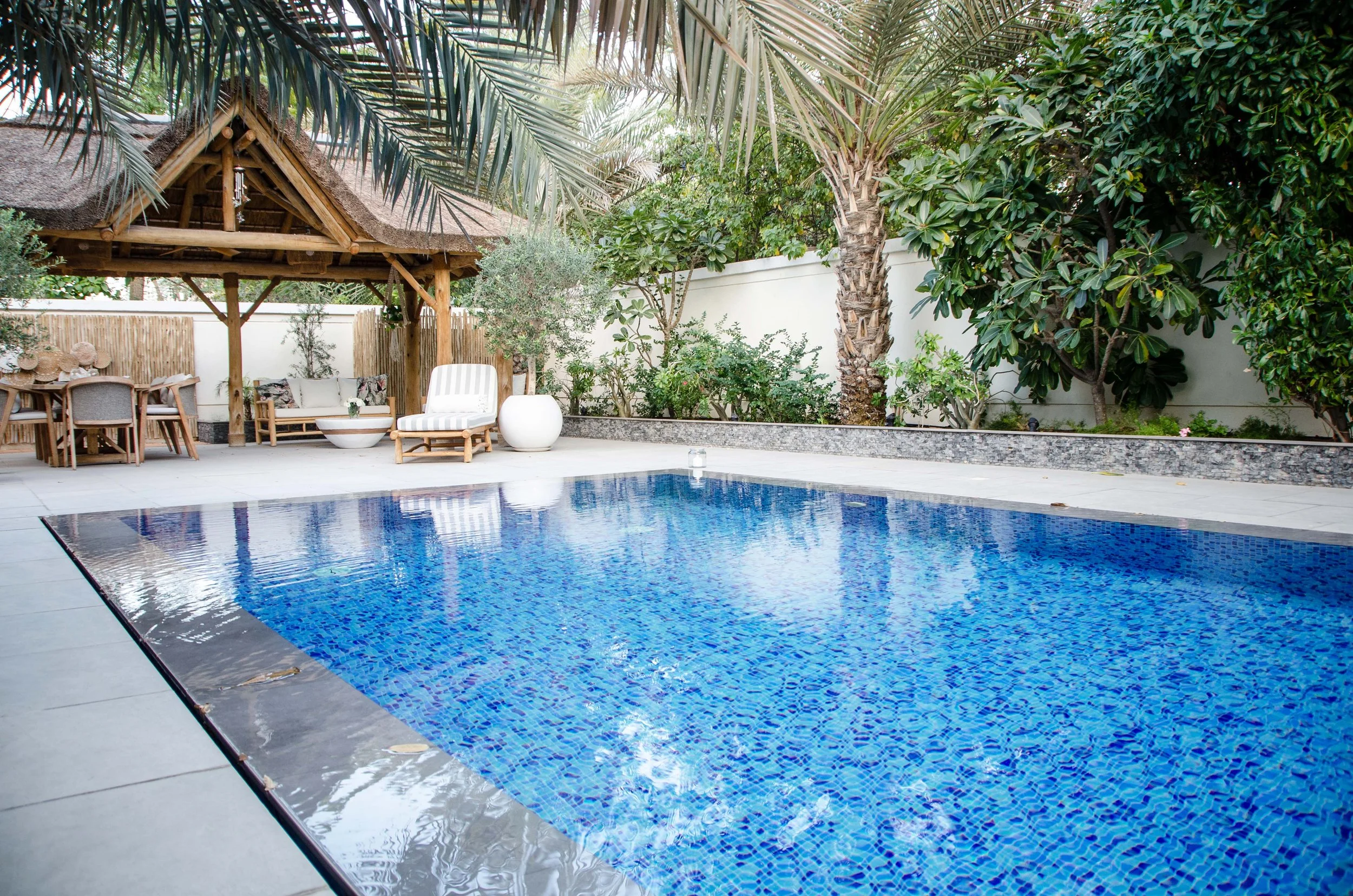 Rectangular blue mosaic-tiled pool with modern paving and lush tropical surroundings