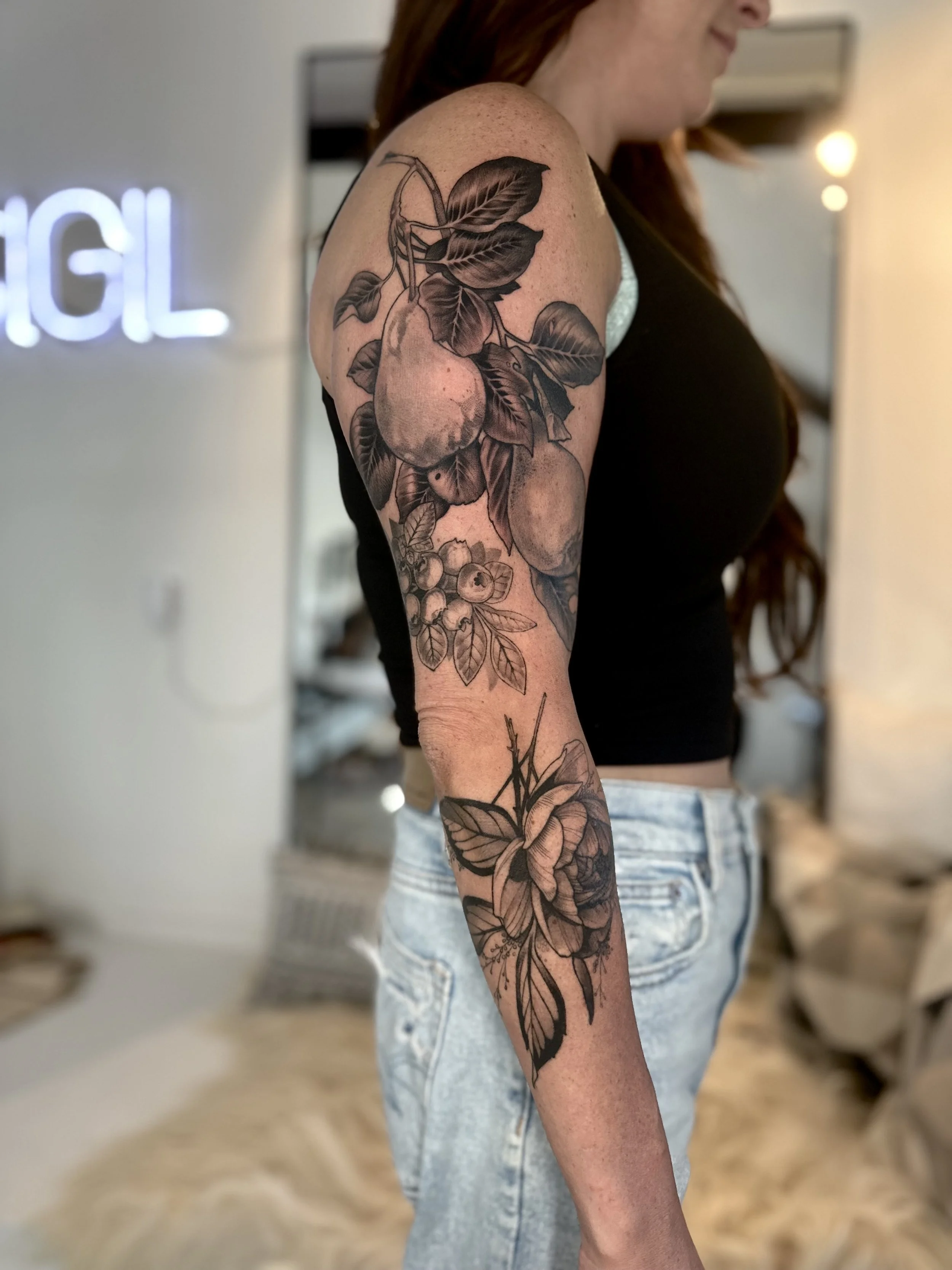 Tattoo of pears, apples, berries, and a lily flower with leaves on the woman's upper arm and forearm.