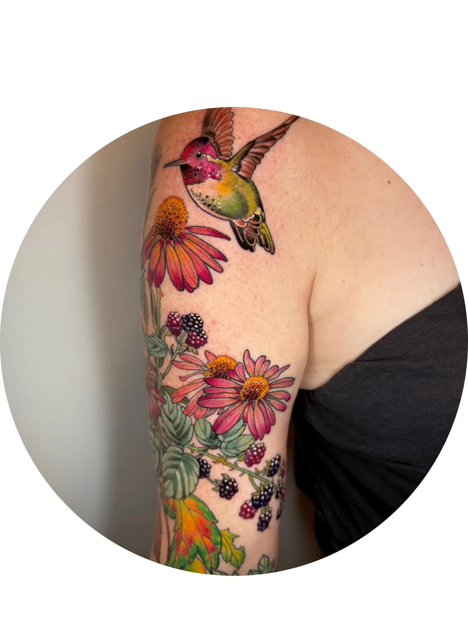 Colorful tattoo of a hummingbird and flowers on person's upper arm and shoulder.