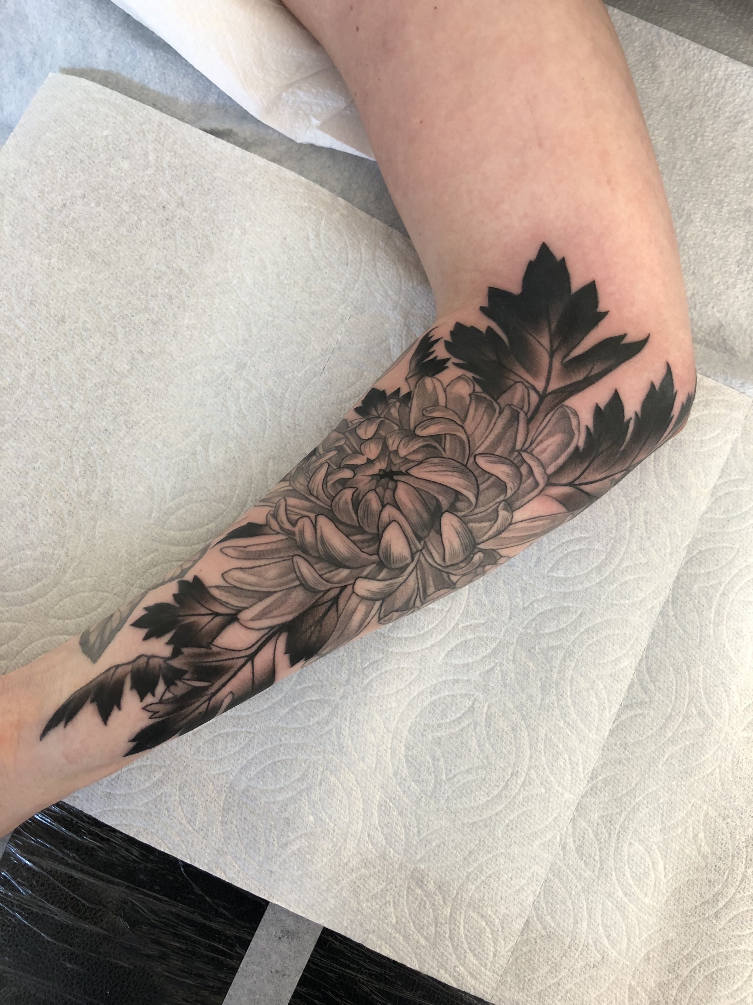 A black and grey floral tattoo on a person's arm featuring a large flower and leaves.