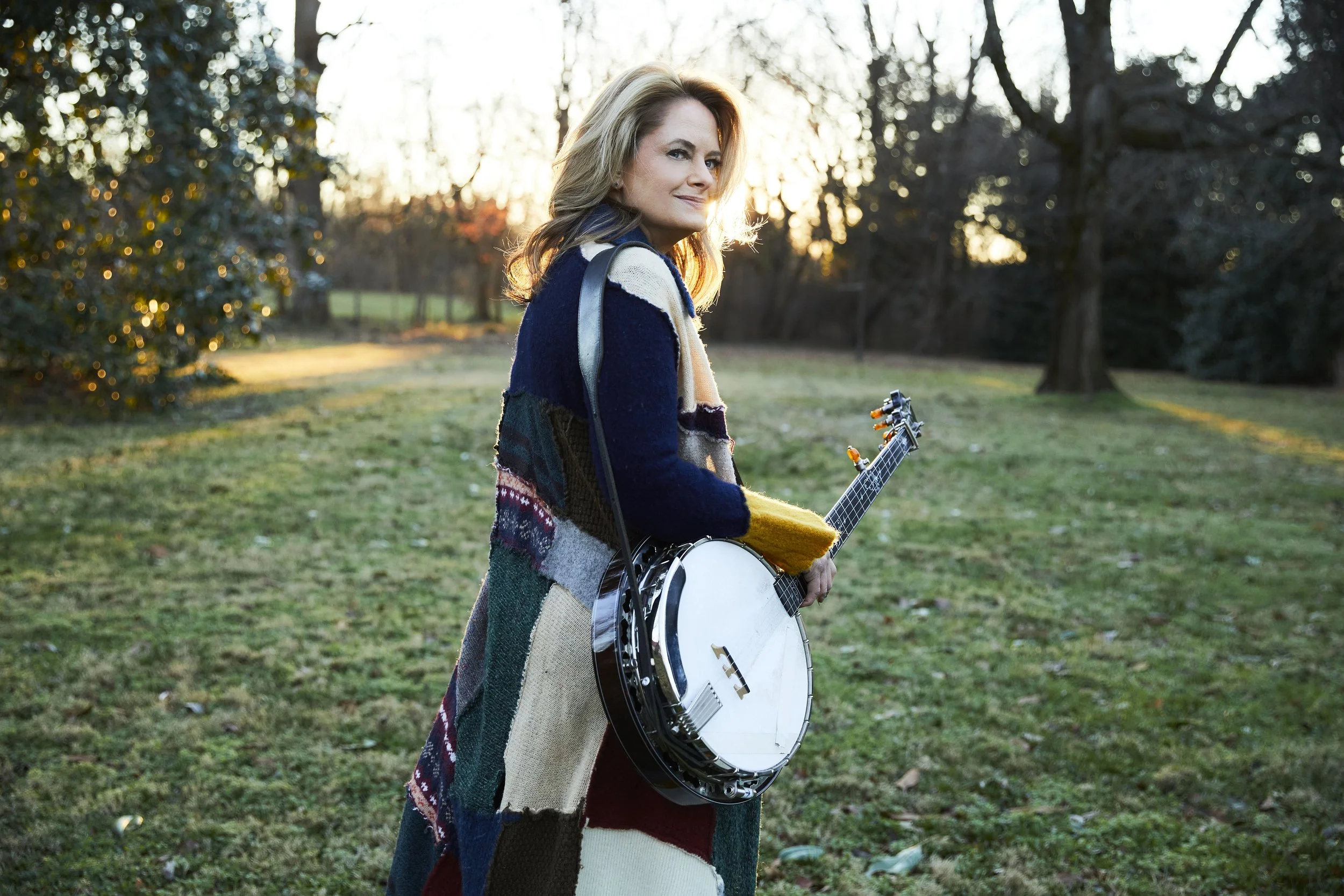 Alison Brown walking with her banjo outside at sunset