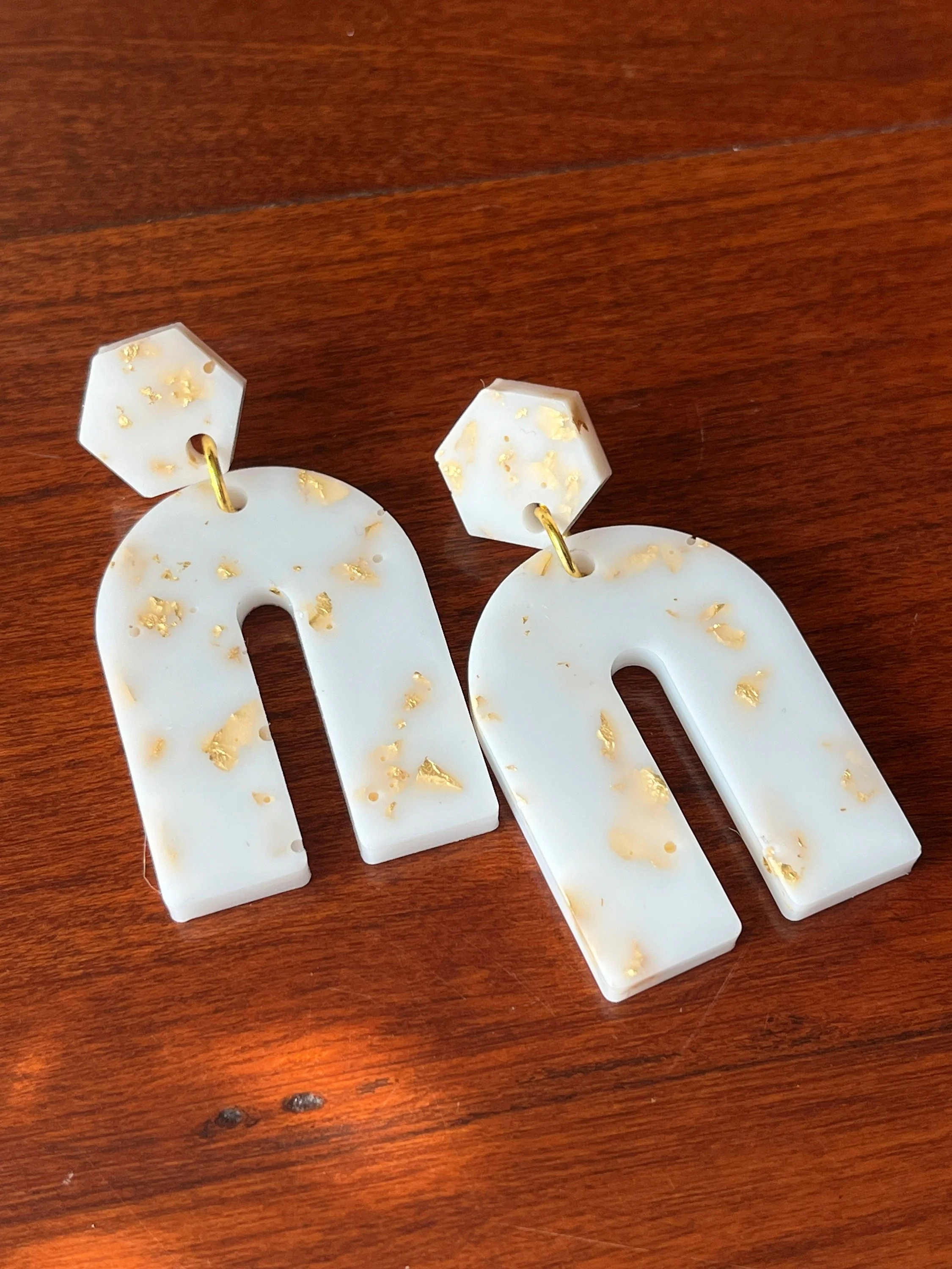 Close-up of white decorative earrings with gold flakes on a wooden surface.