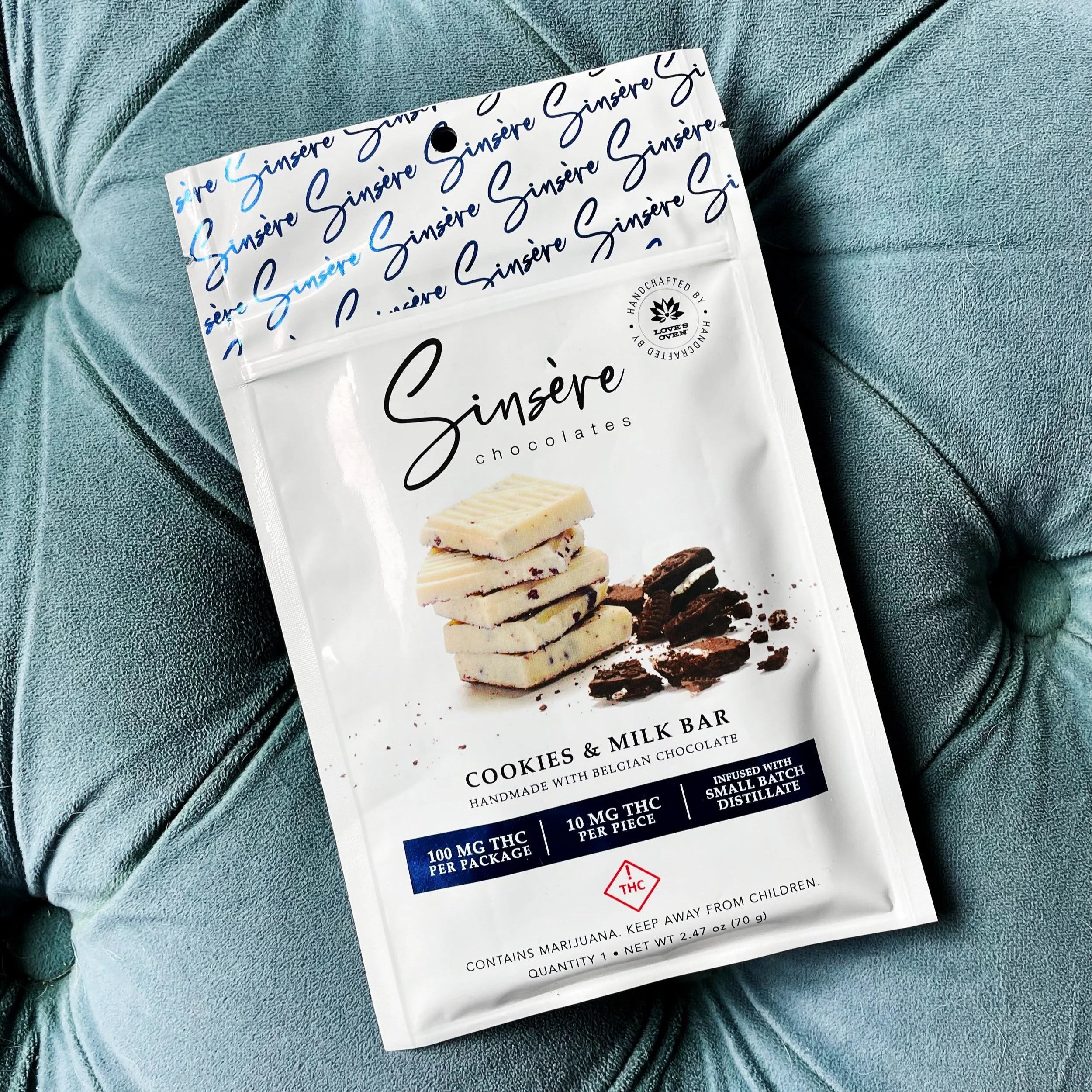 A white bag of cookies and milk chocolate with handwriting text, featuring a stack of assorted white and dark chocolate cookies with visible bits of ingredients on the front.