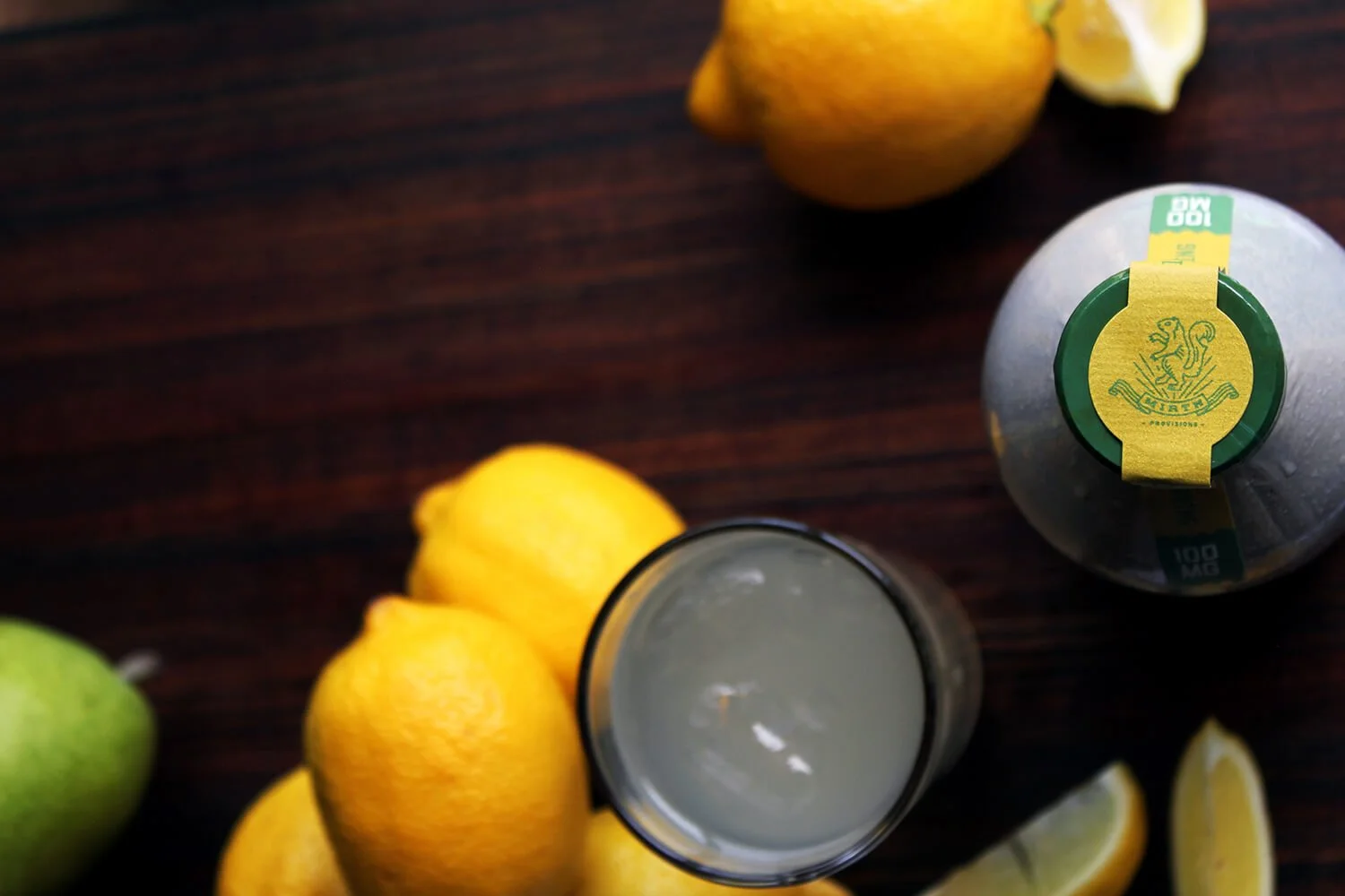 Variety of citrus fruits including lemons, limes, and possibly a grapefruit or orange, with a glass of lemonade on a dark wooden surface.