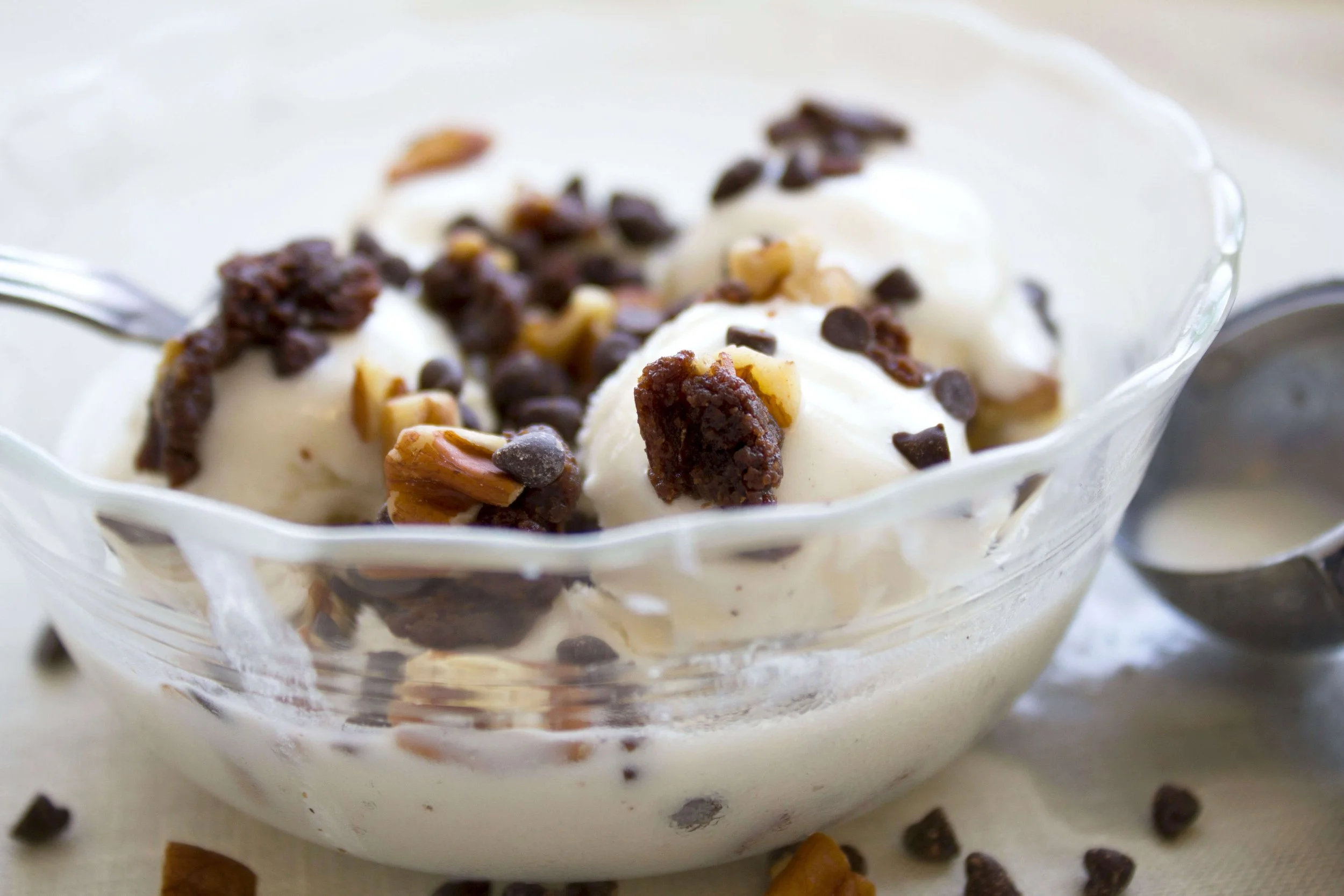 A glass bowl of vanilla ice cream topped with chopped nuts and chocolate chips.