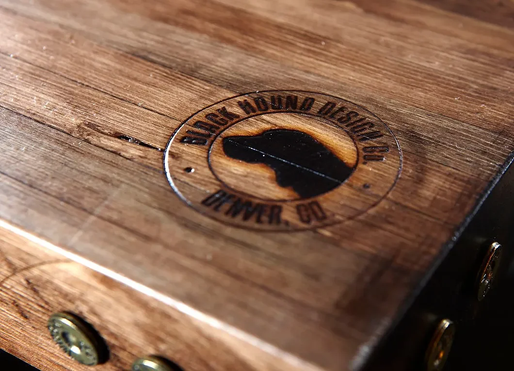 Close-up of a wooden surface with a circular emblem reading "Sanger Molding & Distributing, Denver, CO," featuring a silhouette of a bird.