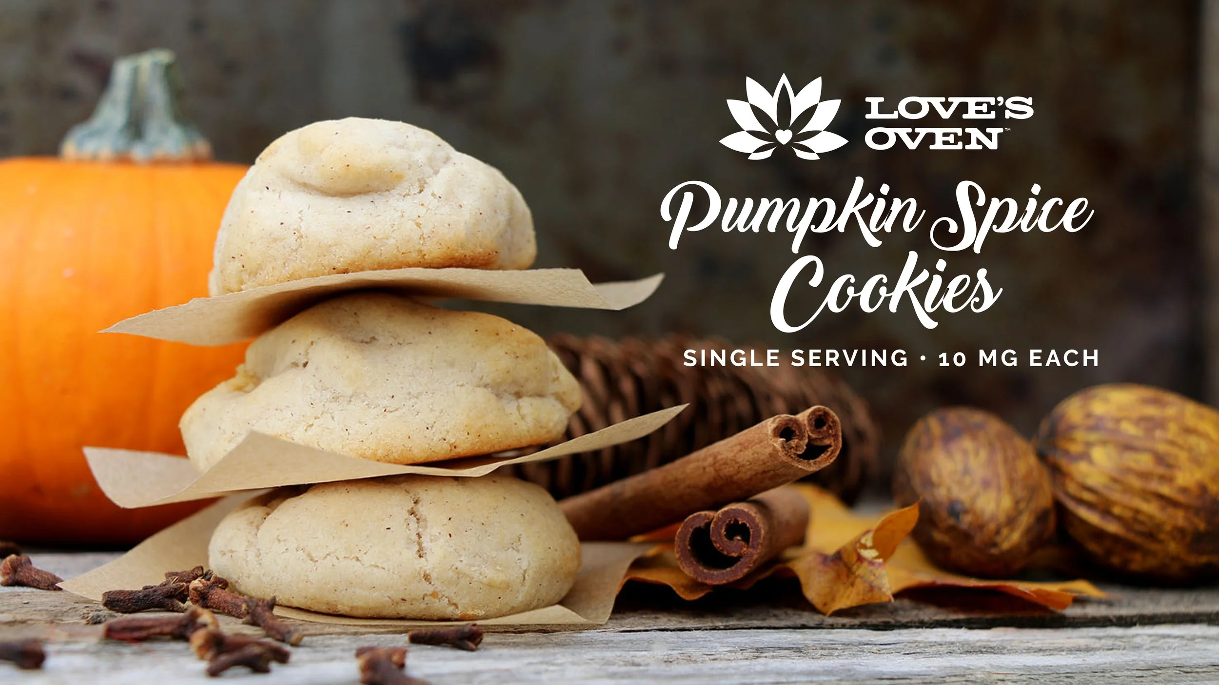 Stacked pumpkin spice cookies on parchment paper with cinnamon sticks, dried leaves, and a pumpkin in the background