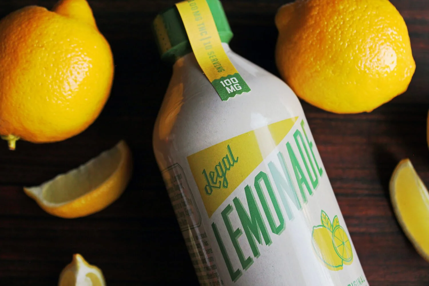 A bottle of Lemonade with lemons and lemon slices on a dark wooden surface.