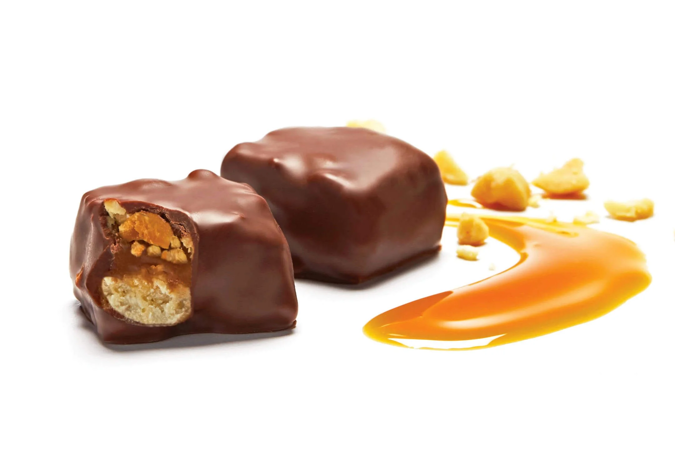 Chocolate-covered caramel and nut confections on a plate with caramel sauce drizzled nearby.