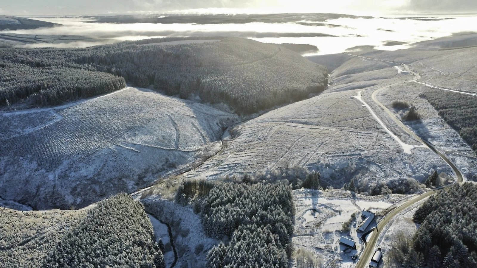 Aerial view of snow-covered hills, fields, roads, and dense pine forests in a winter landscape.