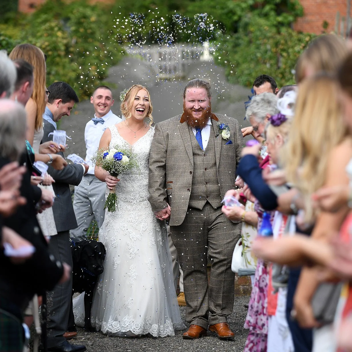 happy couple having confetti thrown as they walk after wedding cermony at sugnall walled garden in staffordshire photographed by wedding photographer chris peach photography