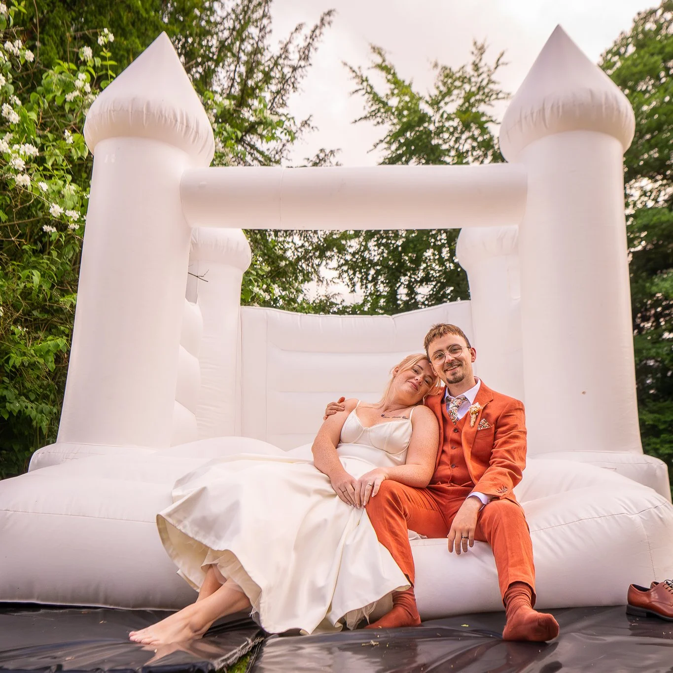 newly married couple pose on the edge of a bouncy castle for couples photoshoot at their wedding reception at dunwood hall estate staffordshire photographed by wedding photographer chris peach photography