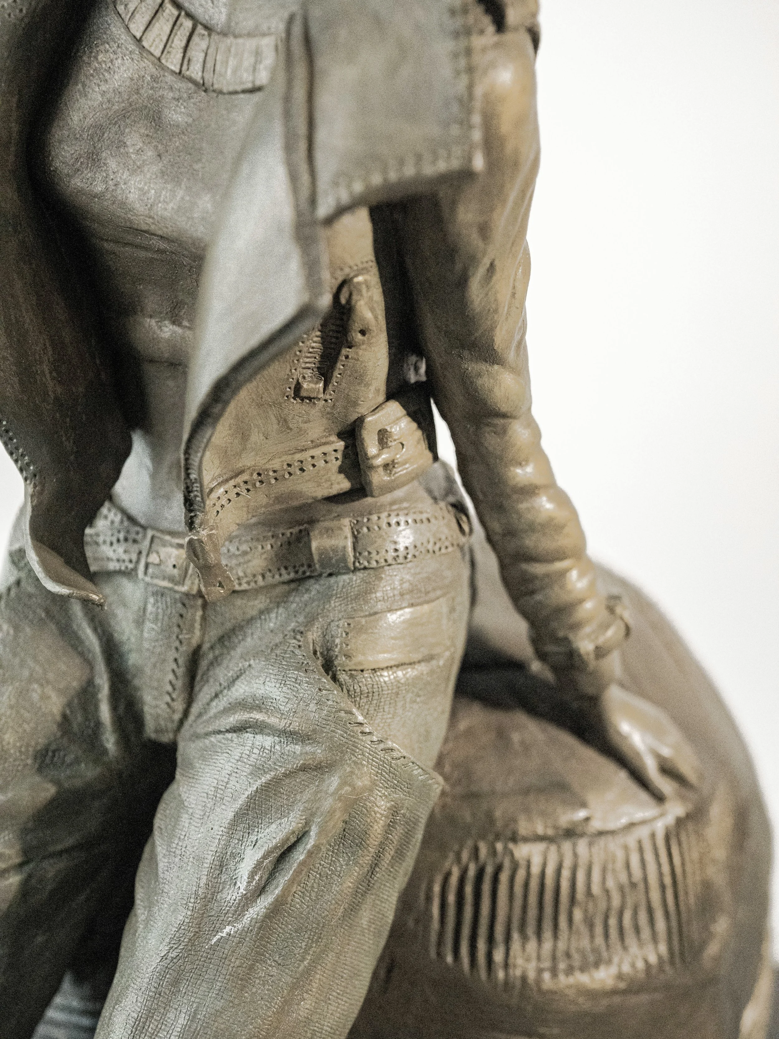 Sculpture Anita de Nervaud Douce Rebelle en grès vitrifié représentant une personne assise sur une sphère texturée, avec une veste ou un vêtement avec une fermeture éclair visible.