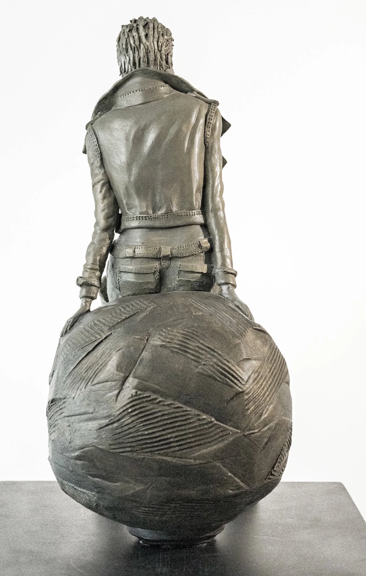 Sculpture Sculpture Anita de Nervaud Douce Rebelle en grès vitrifié représentant une personne vue de derrière, assise sur une sphère texturée, avec une tenue en cuir