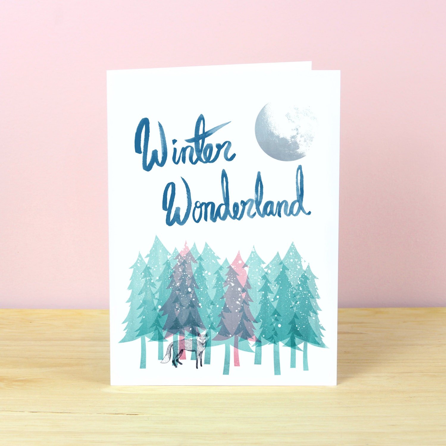 Winter wonderland Christmas card with illustration of snowy forest with a fox amongst pink and green trees