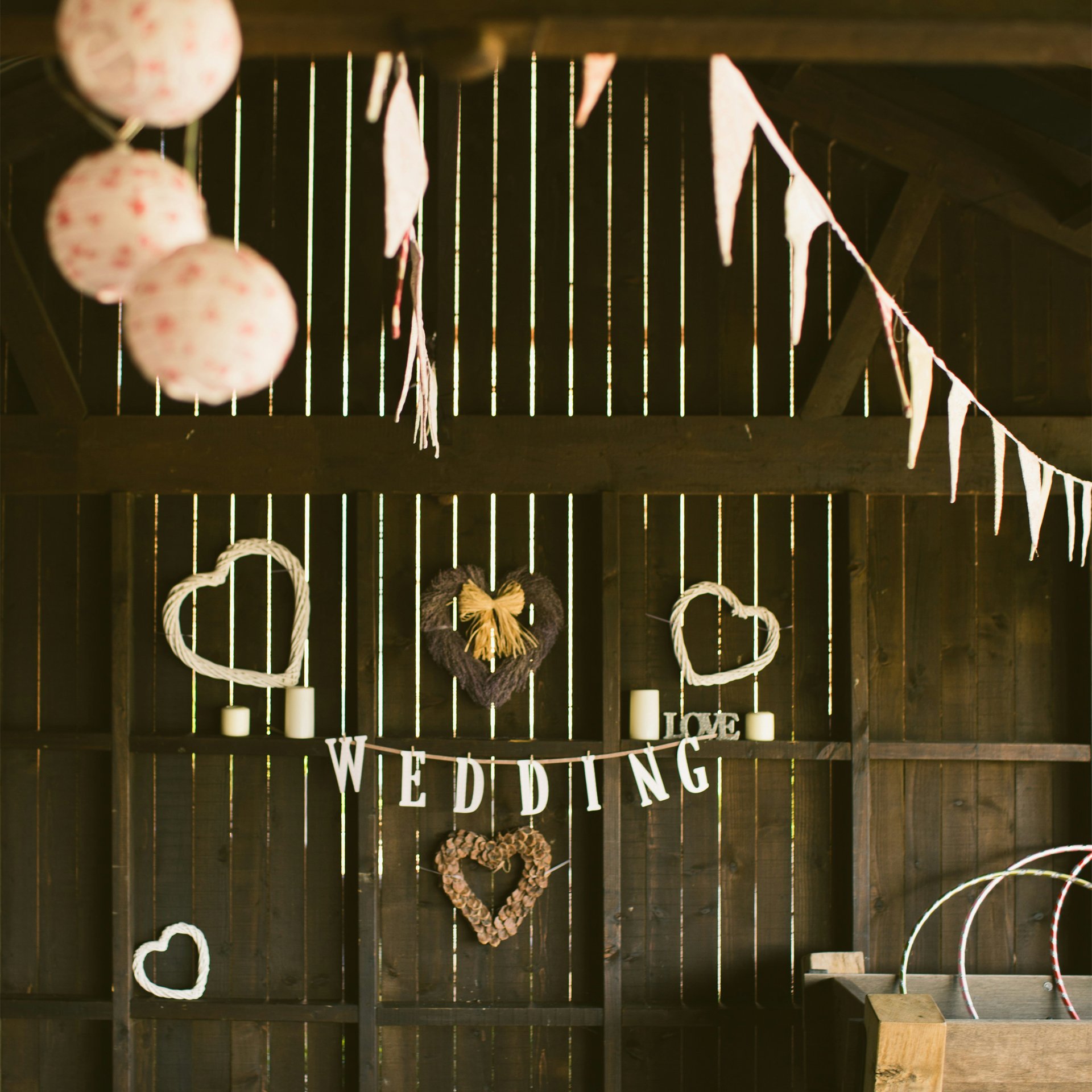 Rustic wedding decoration with heart-shaped wreaths, candles, and a hanging sign that says "WEDDING" in a barn or wooden structure.