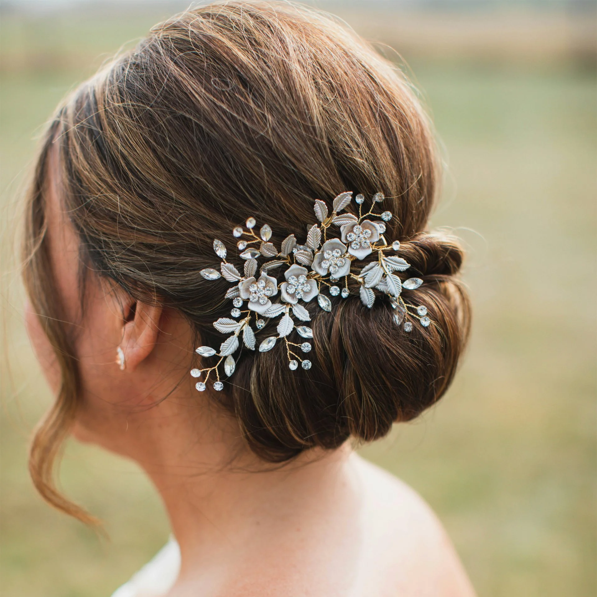 A woman's updo hairstyle decorated with a silver floral hairpiece with leaves and flowers, outdoors with a blurred background.