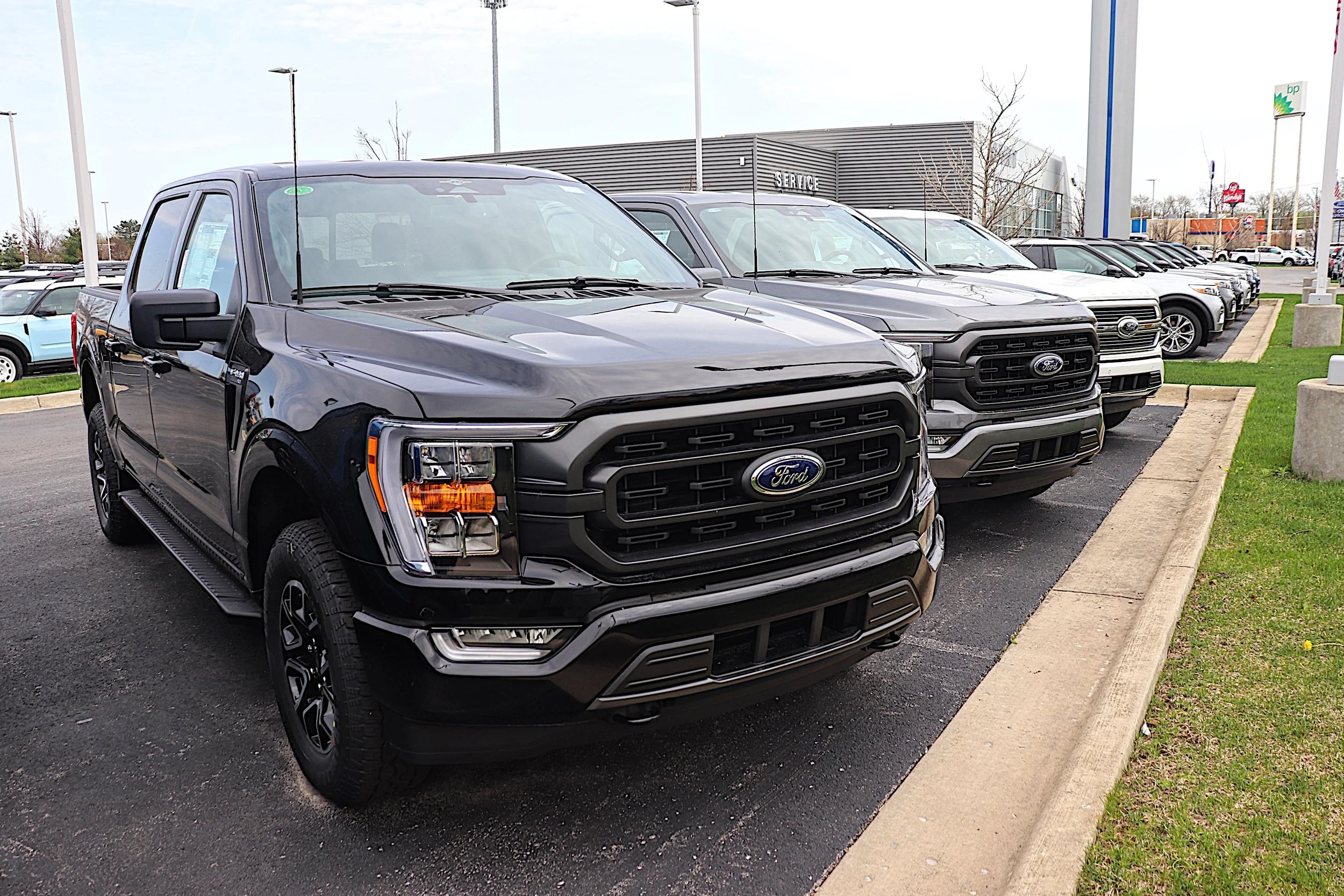 Line of black and gray Ford pickup trucks parked at a dealership lot.