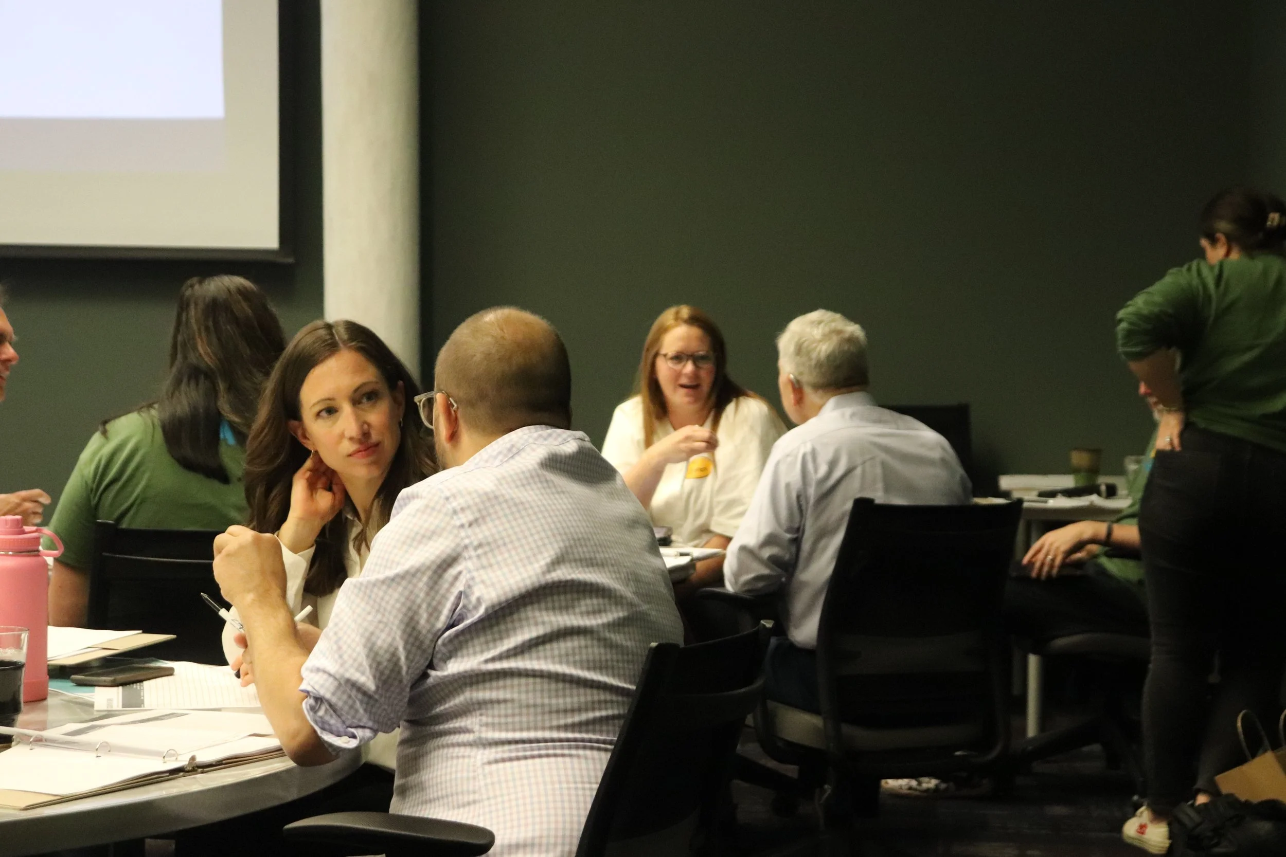 Group of people engaged in discussion in a conference room with tables and chairs.