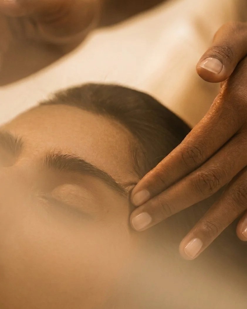 A person receiving a facial massage or treatment, with their eyes closed and a gentle hand applying pressure to their forehead.