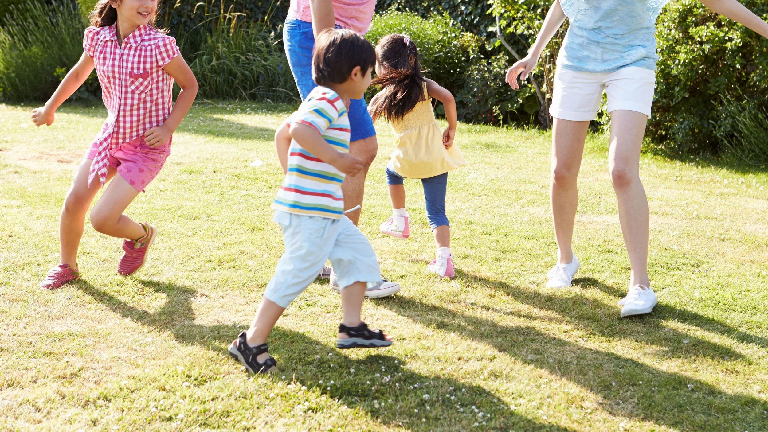 Children playing and running on a grassy area outdoors with an adult supervising.