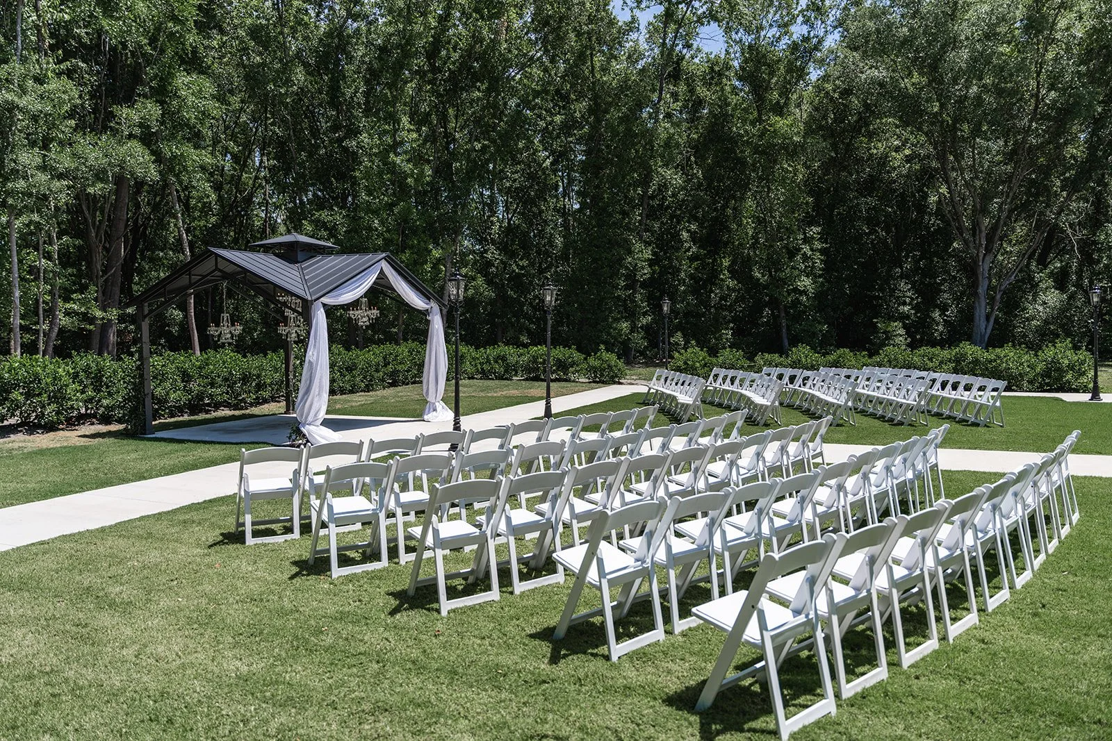 Outdoor wedding ceremony setup with white folding chairs and a gazebo with draped fabric.