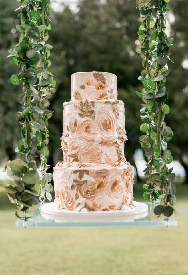 Three-tier floral cake on swing with greenery, outdoor background.