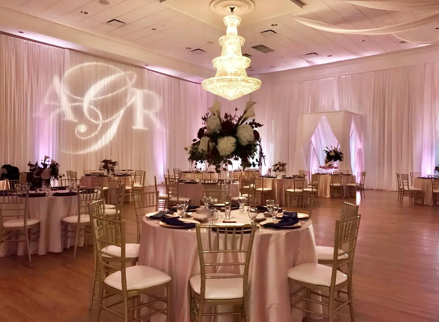 Picture perfect wedding at The Regent. We provided Wall Draping, Draped 4 Post Canopy w/Suspended Cake Stand, Gold Chiavari Chairs, Monogram Gobo Projection, Up Lighting, & Hold Chargers. ————————&m