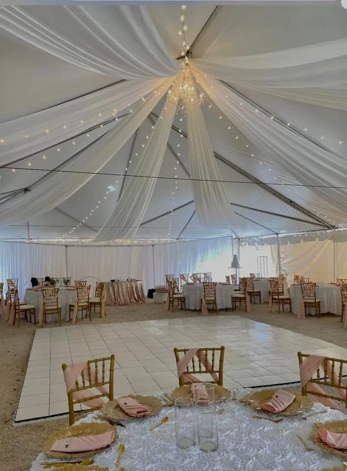 Decorative wedding tent with draped fabric and string lights, set tables with gold chairs and pink napkins, and a central dance floor.