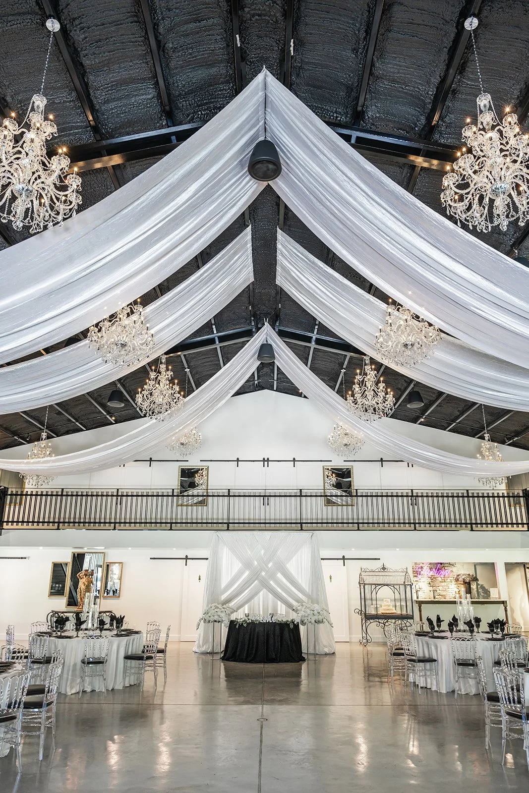 Elegant event hall with white draped ceiling and chandeliers, featuring decorated tables and a central arch.