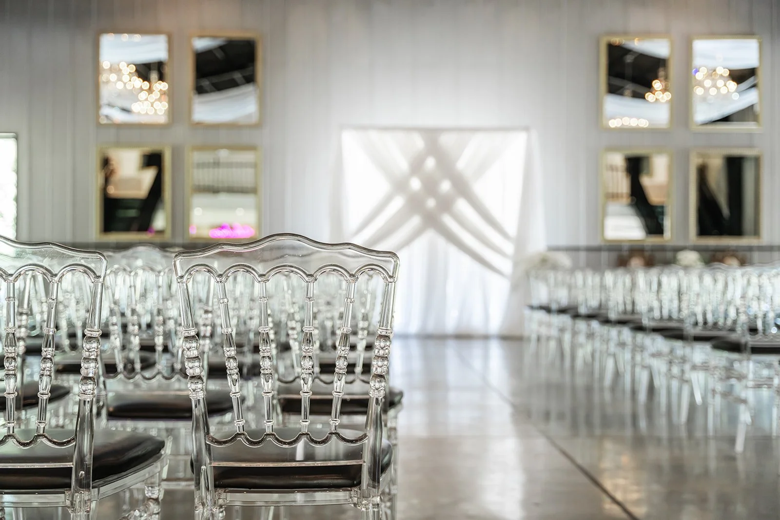 Empty event venue with clear chairs facing a lit backdrop and mirrors on the wall.