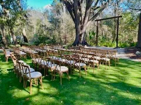 Outdoor wedding ceremony setup with wooden chairs on grass facing an arch and trees.
