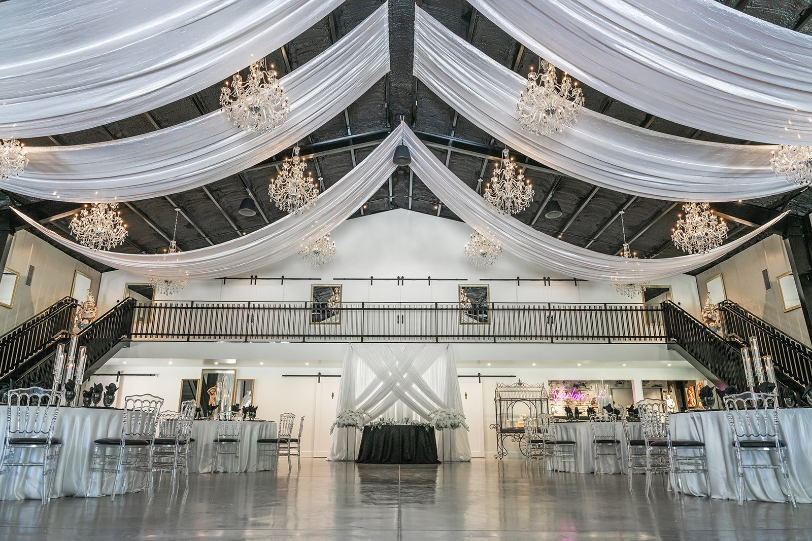Elegant wedding venue with draped ceiling, chandeliers, mirrored tables, and sleek chairs.