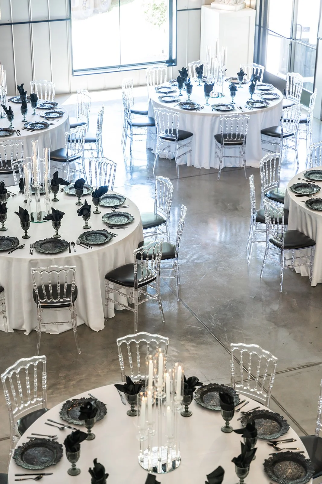 Elegant dining setup with round tables, white tablecloths, black napkins, crystal chairs, and tall candles.