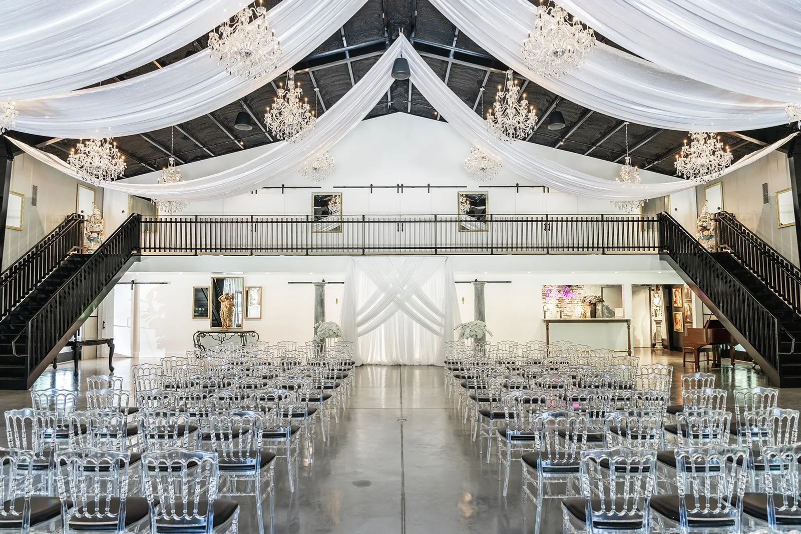 Elegant wedding venue interior with clear chairs and white draped ceiling.
