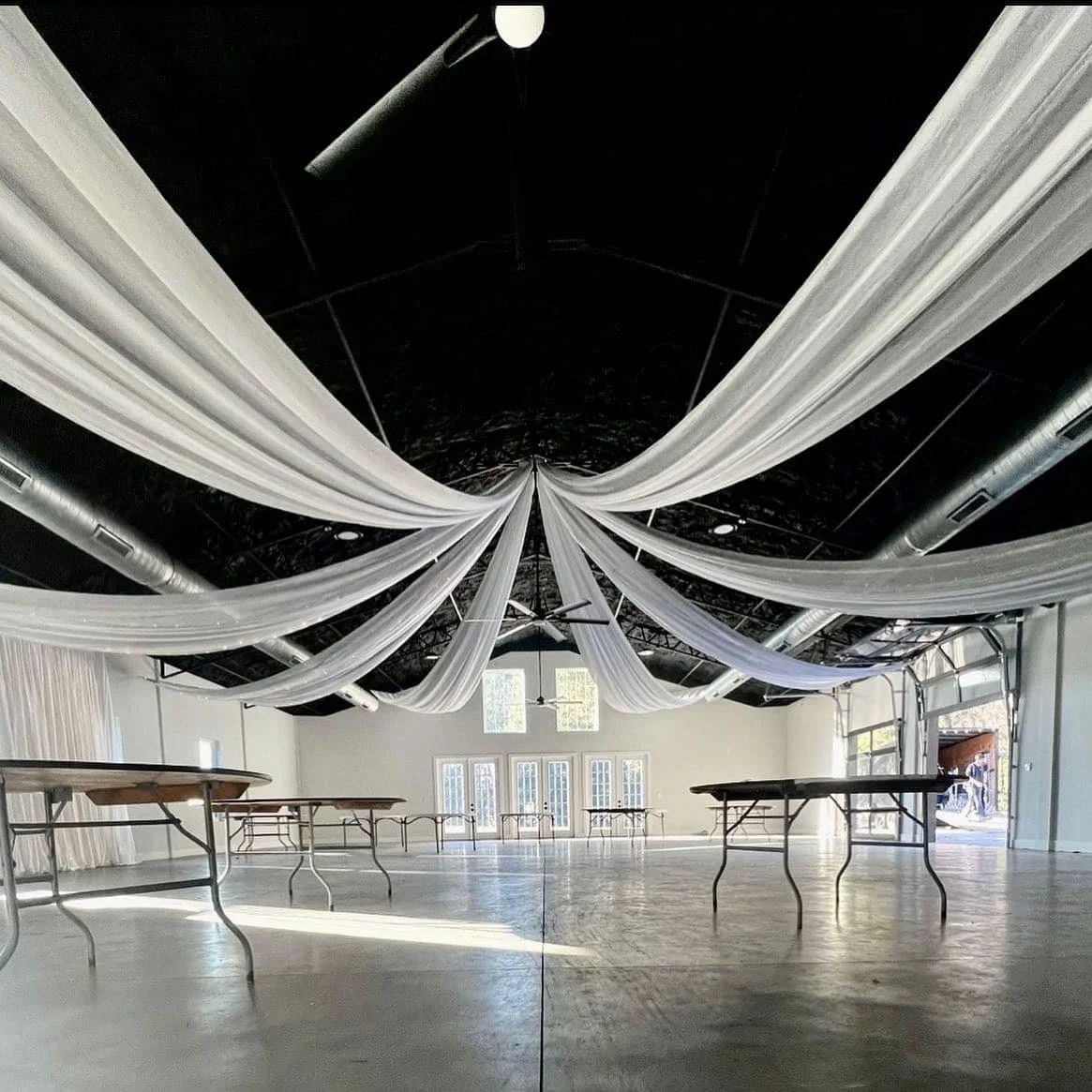 Large event hall with white drapery on ceiling, empty tables, and industrial design elements.