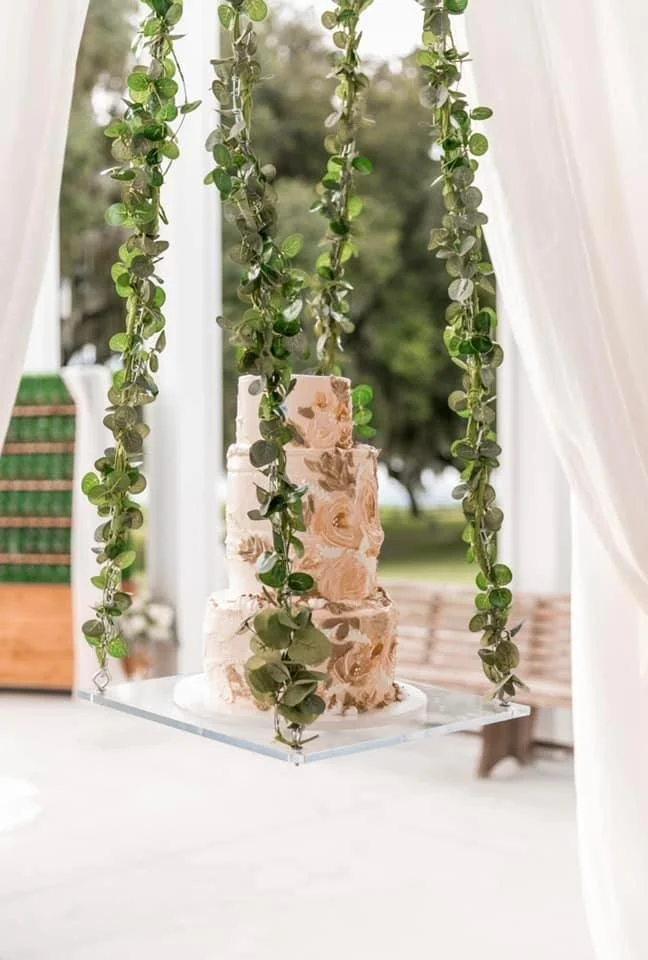 Three-tier floral cake on a hanging platform with greenery.