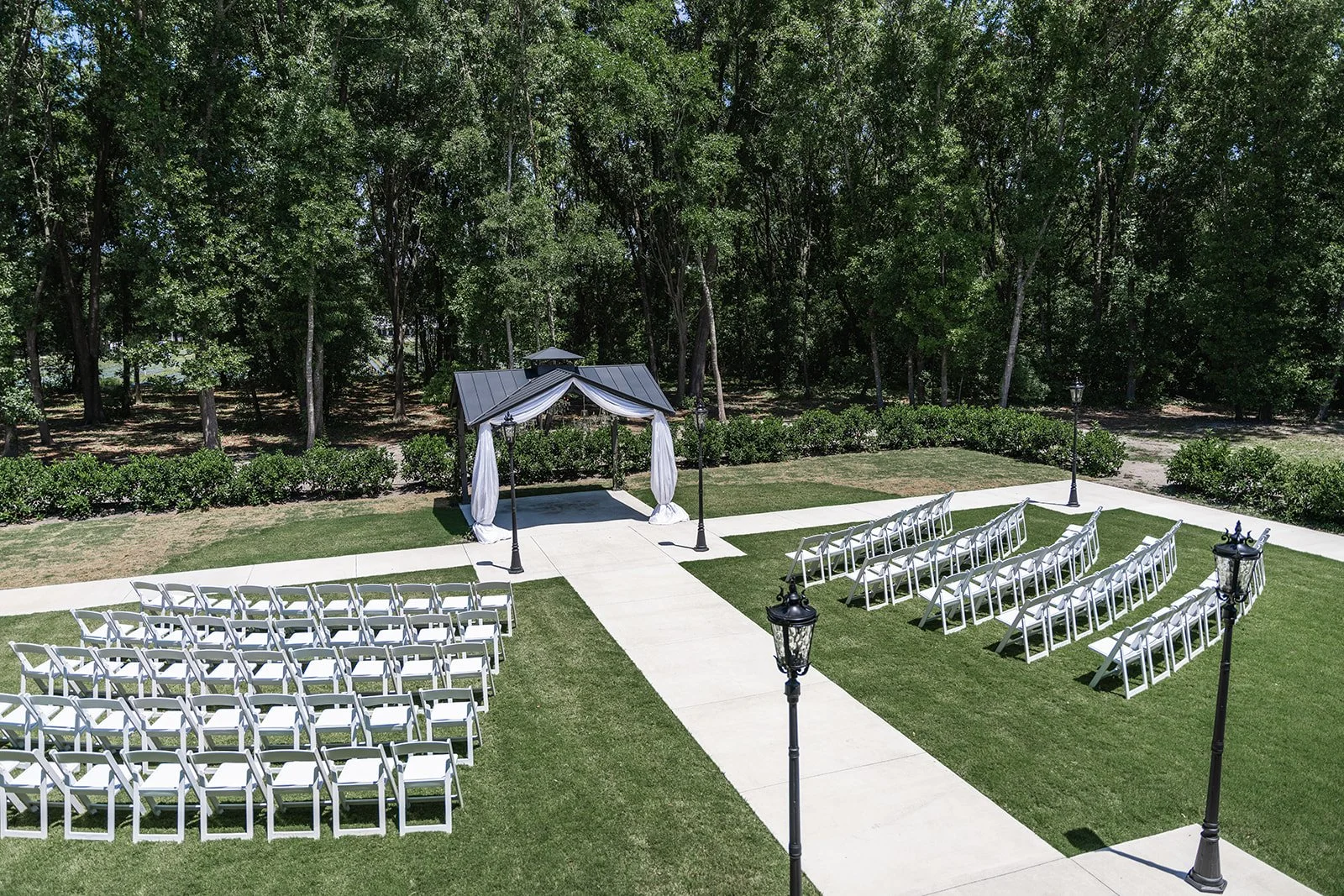 Outdoor wedding ceremony setup with white chairs and a decorated gazebo, surrounded by trees.