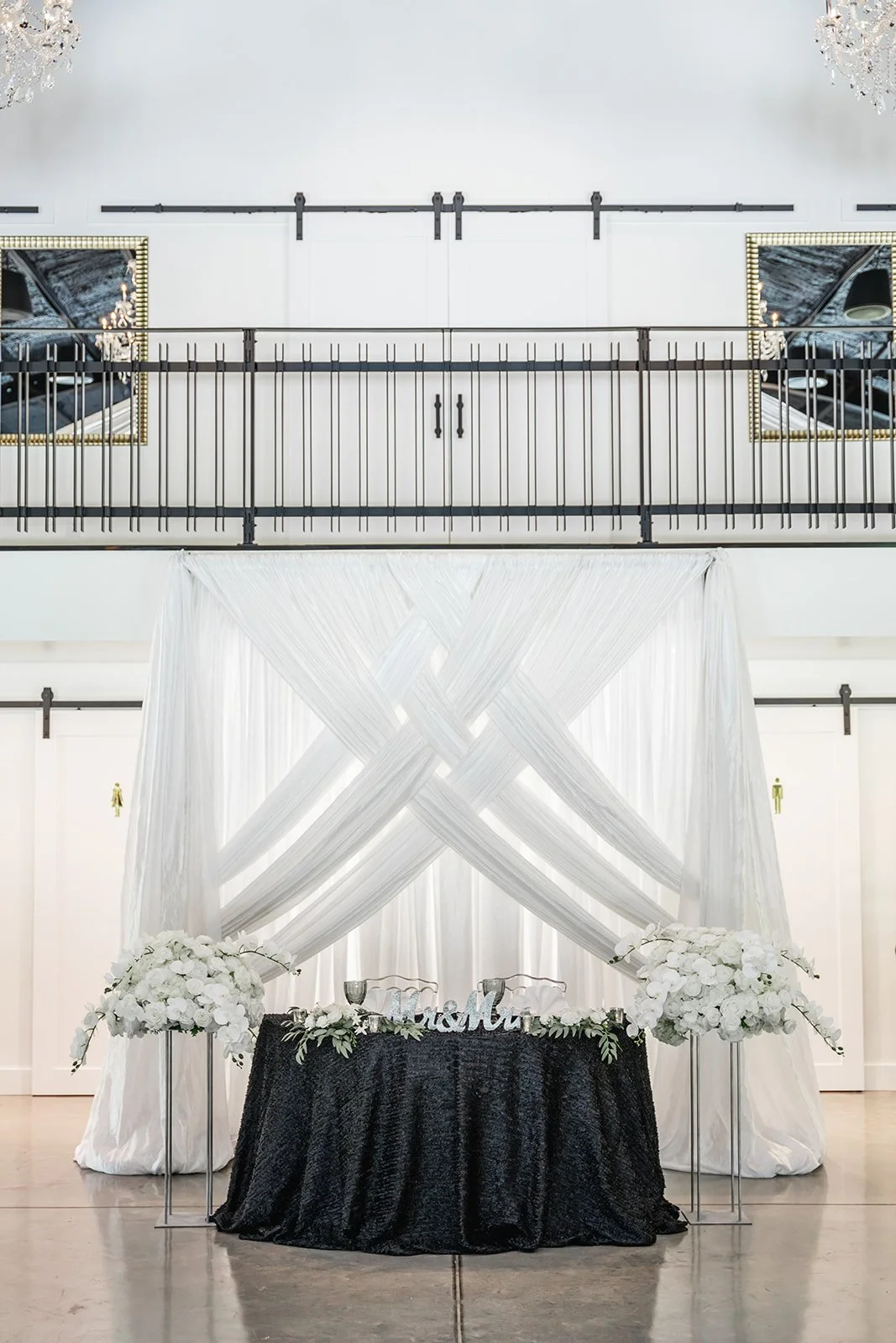 Elegant wedding reception backdrop with white drapery, black tablecloth, and floral arrangements.