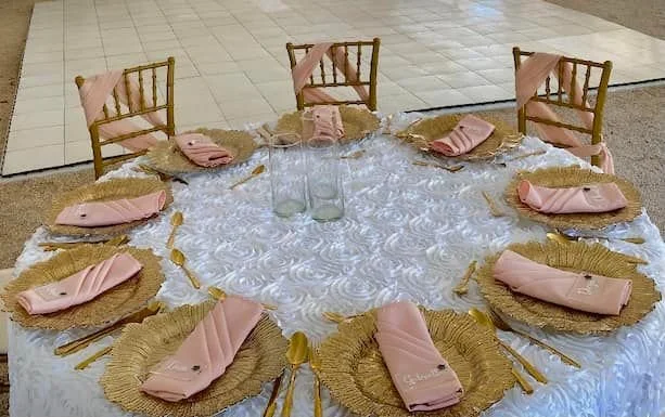 Elegant table setting with gold plates and pink napkins arranged for a formal event.