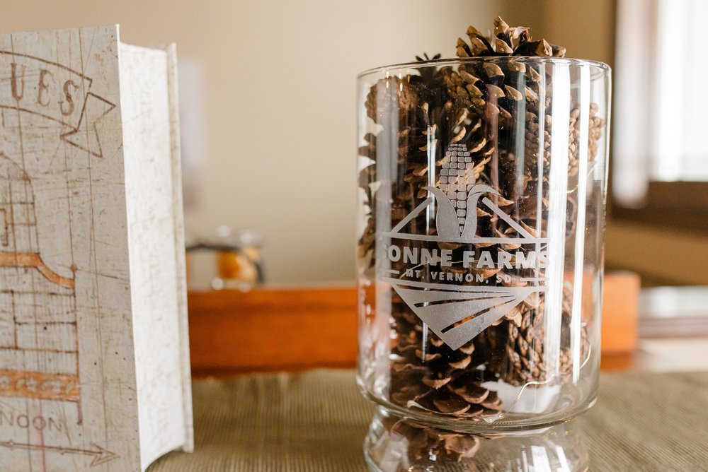 A glass cylinder filled with pinecones, labeled with Sonne Farm's Logo.