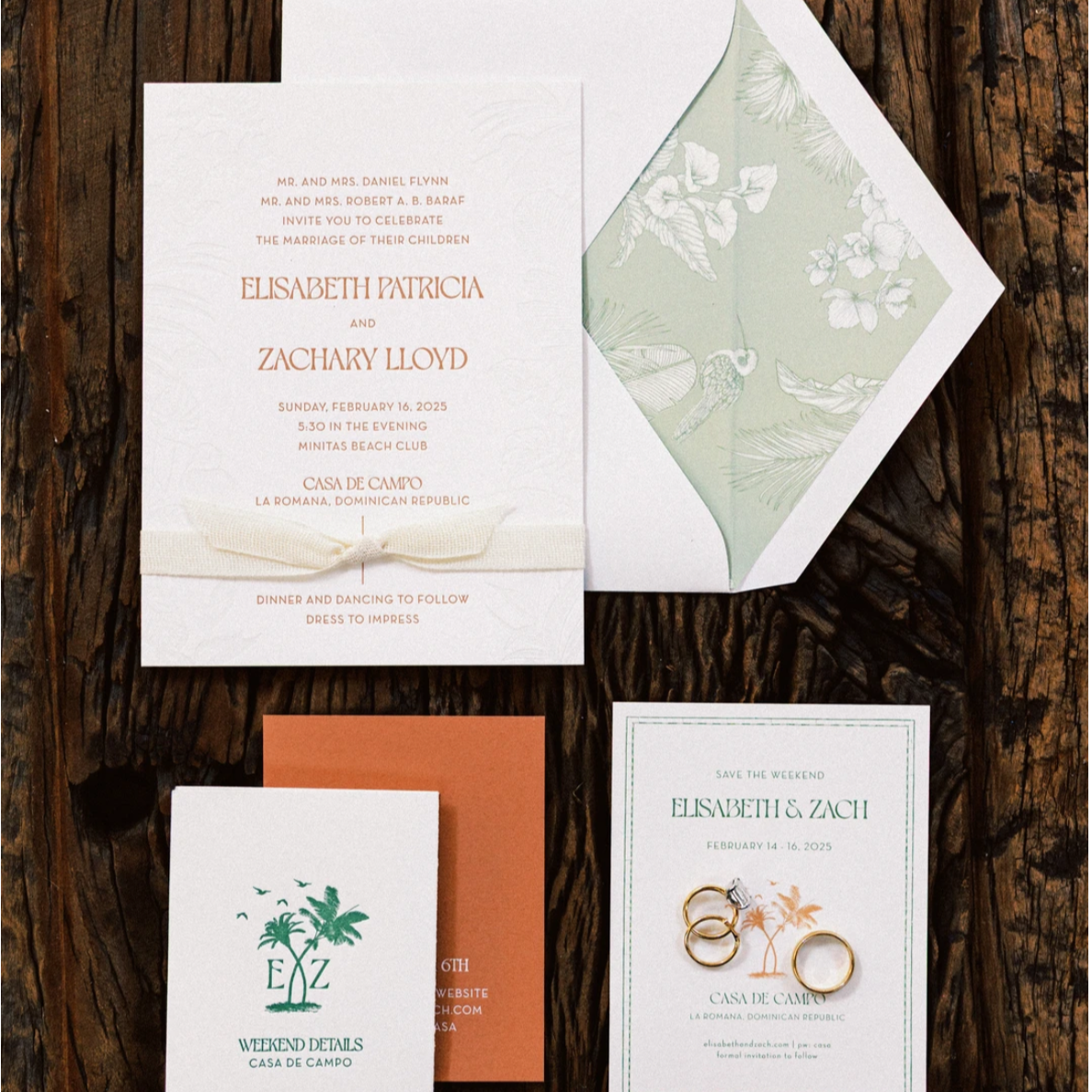 Wedding invitation suite with an envelope, RSVP card, and save the date card, all featuring tropical and botanical themes, placed on a wooden surface.