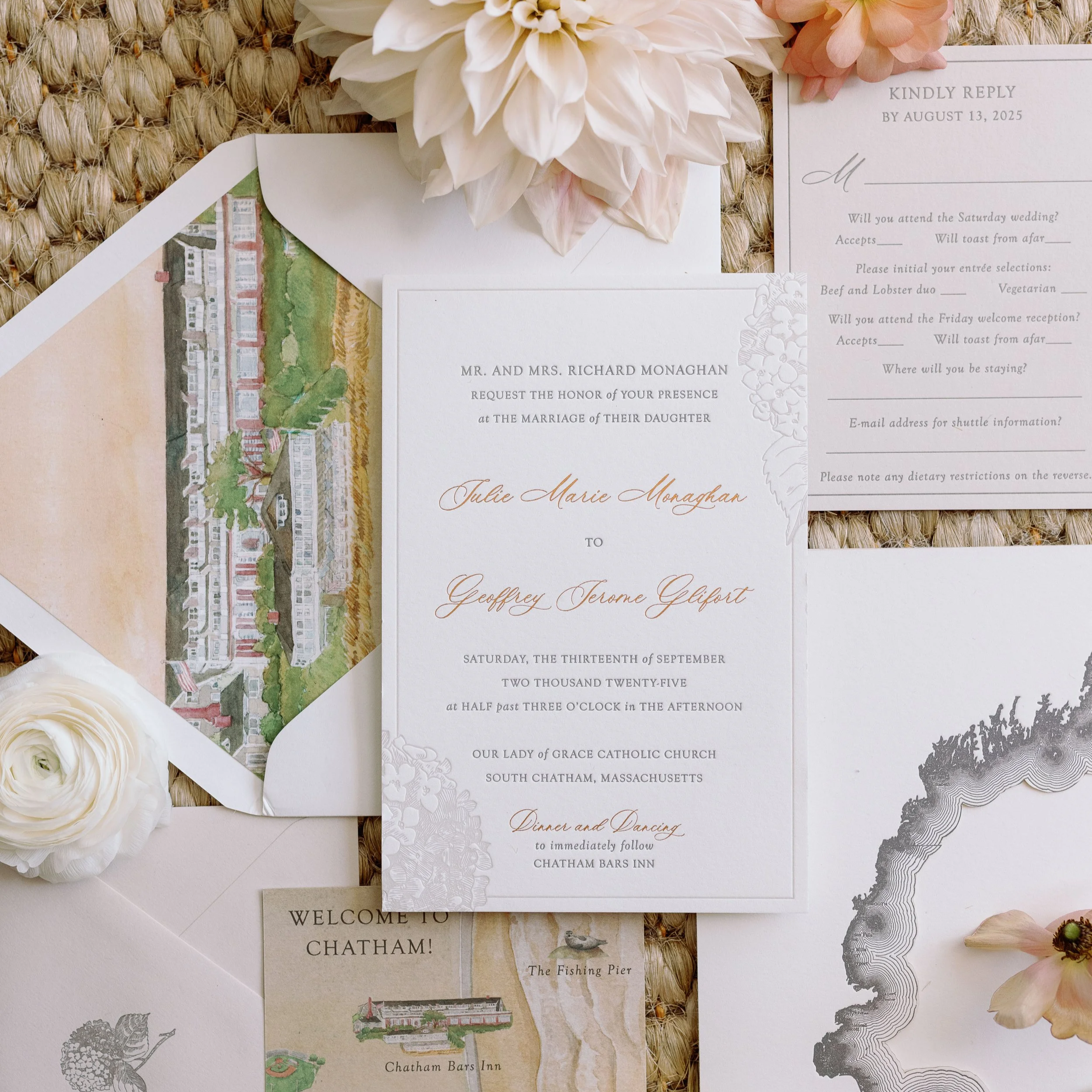 Wedding invitation suite with floral accents, an RSVP card, an illustration of a building, and a welcome note, all arranged on a woven surface with flowers.