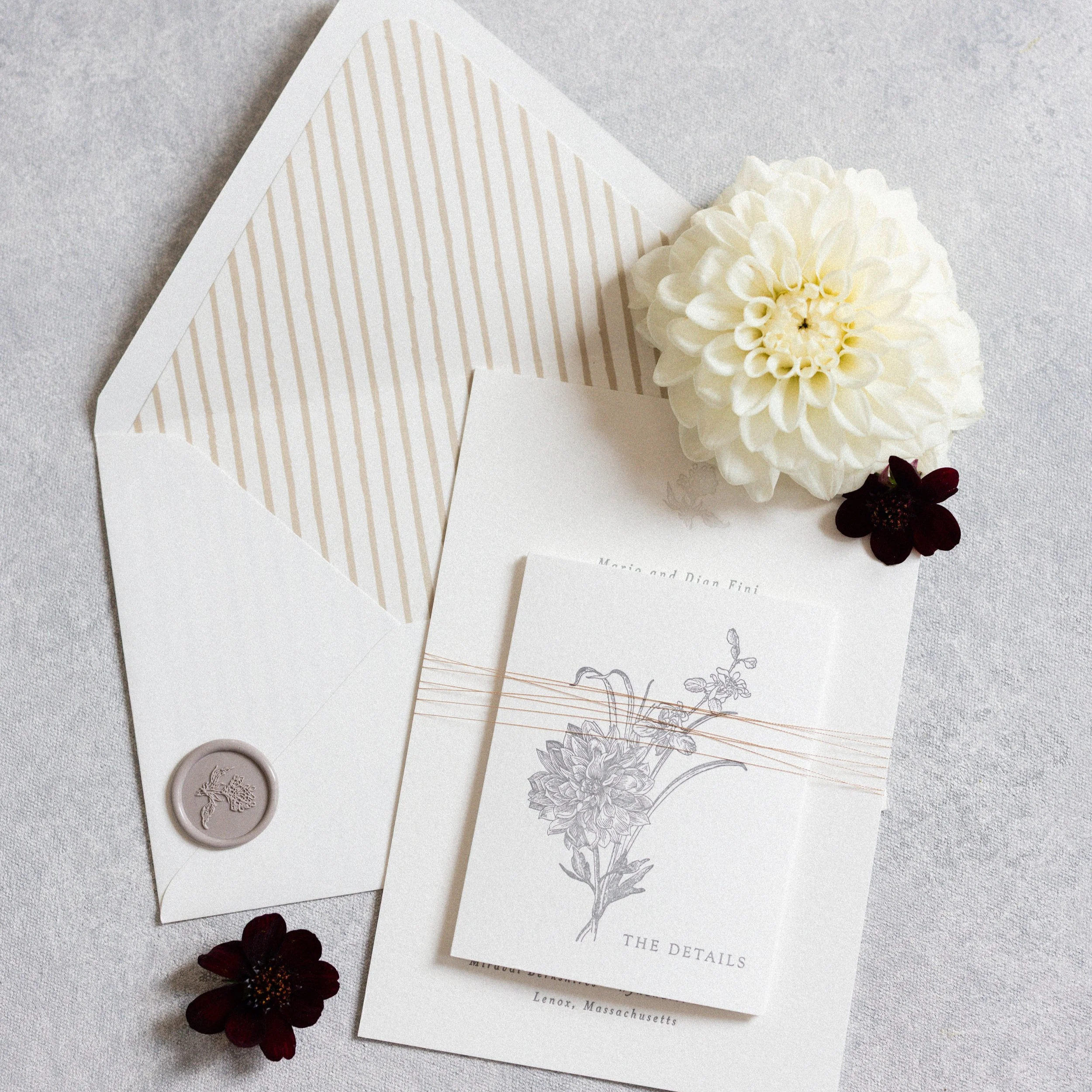 Wedding invitation suite with a large white flower and dark red flowers on a textured gray surface.