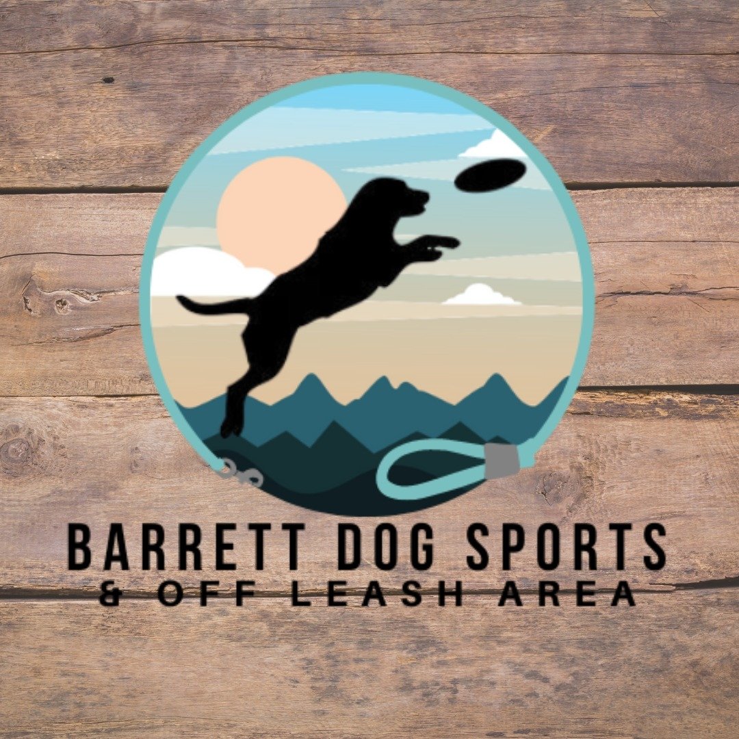 A logo for Barrett Dog Sports & Off Leash Area featuring a silhouette of a dog jumping and catching a frisbee against a mountain and sky background, with a wooden texture behind.