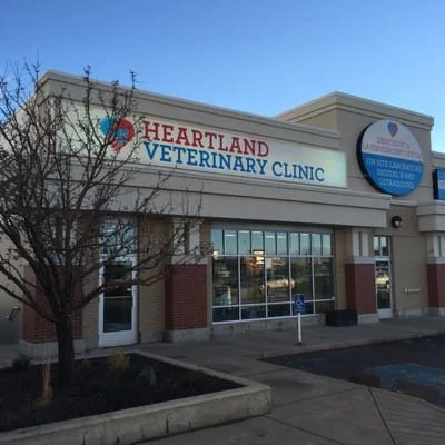 Exterior of Heartland Veterinary Clinic with a sign displaying the clinic's name, a logo, and a blue circle indicating services, under a clear sky.