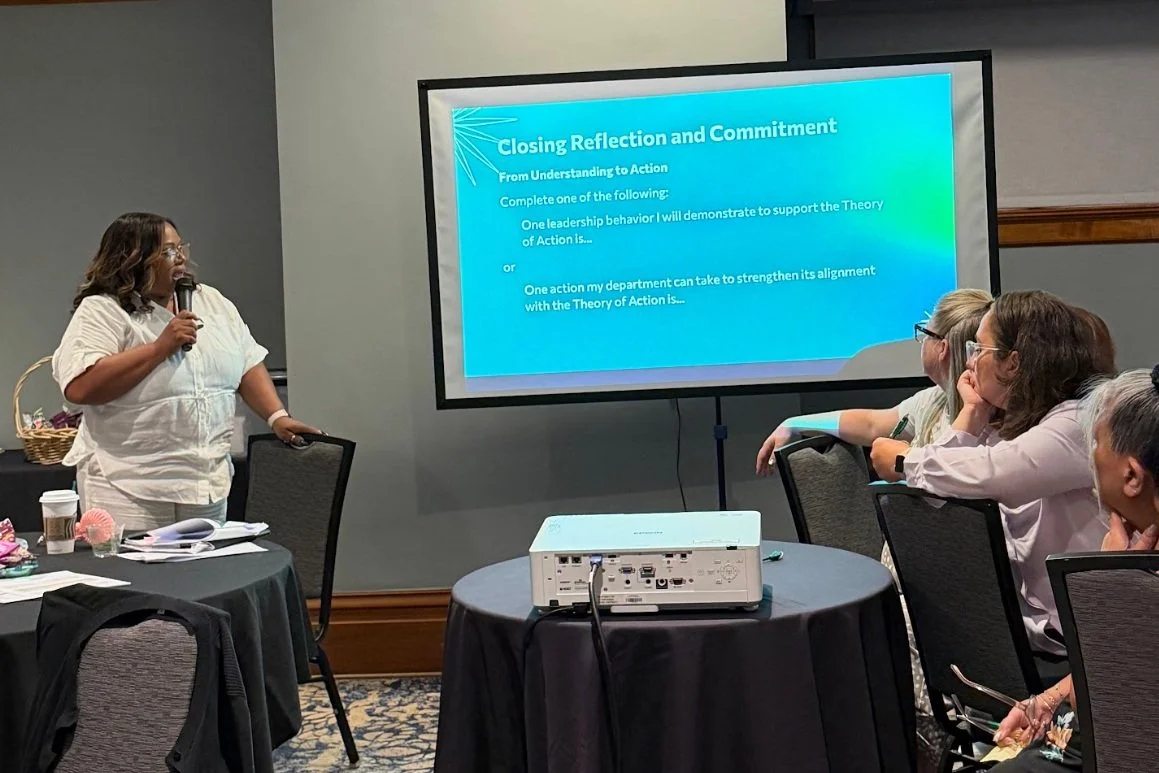 Photo of Assistant Superintendent Tonya Trim with a microphone in front of a meeting room explaining a “Closing Reflection and Commitment” slide shown on a projector screen.